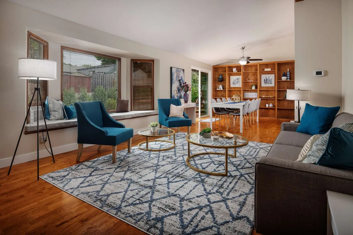 This image shows a relaxing, open living area with blue accent chairs, round coffee tables, and large windows that let in natural light. The dining area is visible, offering a glimpse of a spacious and comfortable environment suitable for both relaxation and informal meetings.